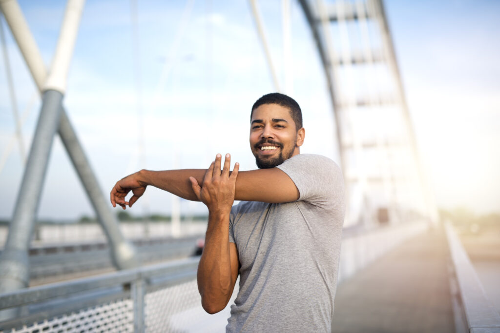 Attractive smiling sportsman warming up his body for an outdoor training.